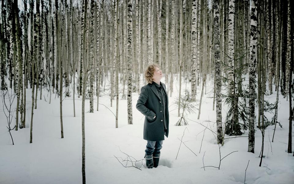 Santtu-Matias Rouvali standing in the snow surrounded by bare trees, looking up towards the sky