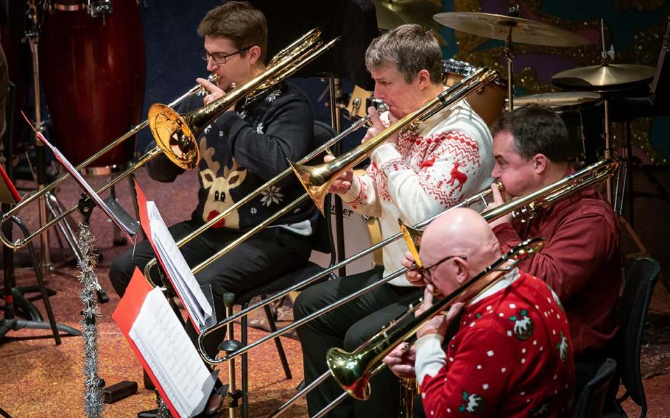 Four trombone players with their instruments wearing Christmas jumpers