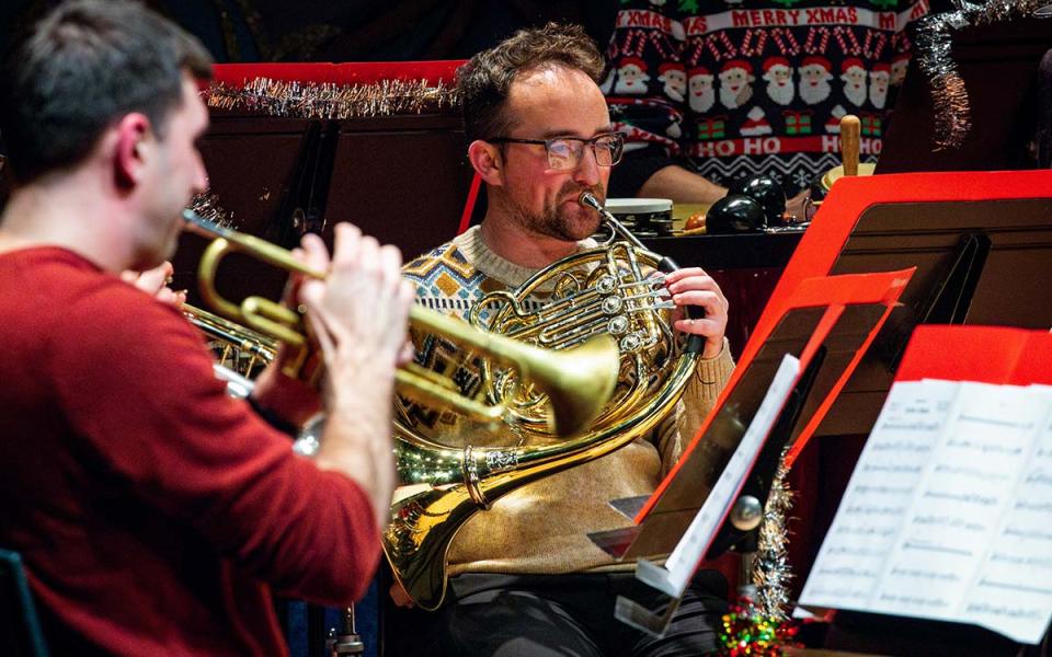 A horn player and trumpet player against a festive backdrop