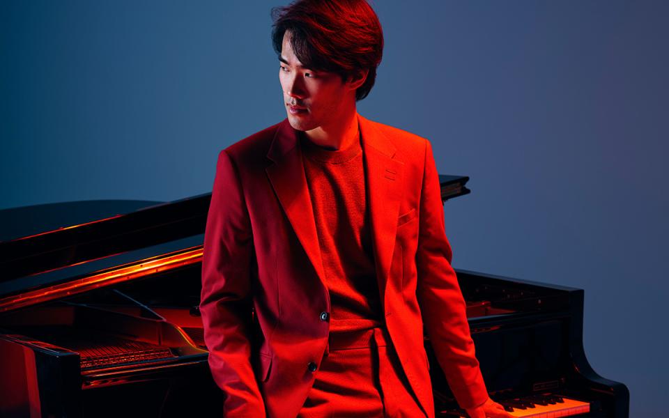 Bruce Liu leaning against a piano, in red lighting