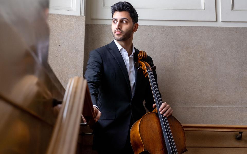 Kian Soltani holding a cello and looking outwards out of a window