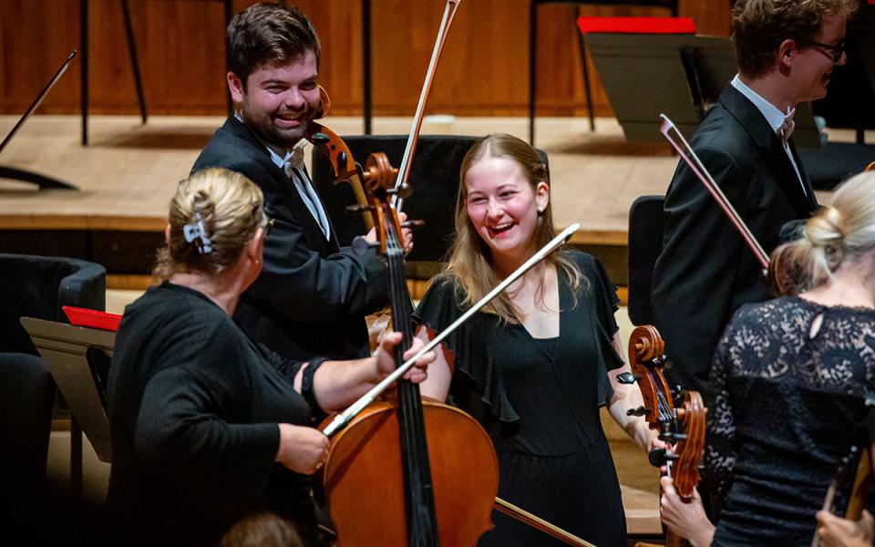 Three cellists smiling at each other on stage at Royal Festival Hall