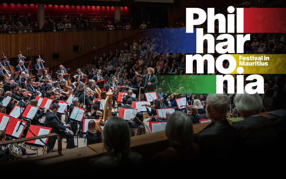 Wide shot of Santtu-Matias Rouvali conducting the Philharmonia Orchestra at Royal Festival Hall, with the audience behind them. There is a designed 